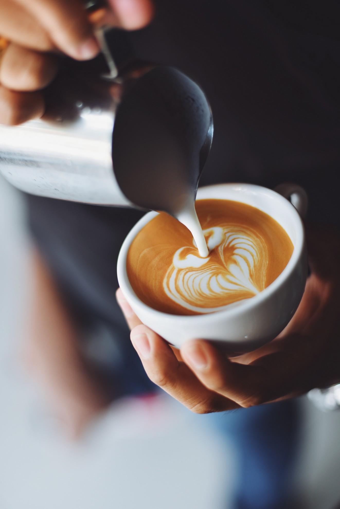 Un serveur en train de verser du lait dans une tasse de café.