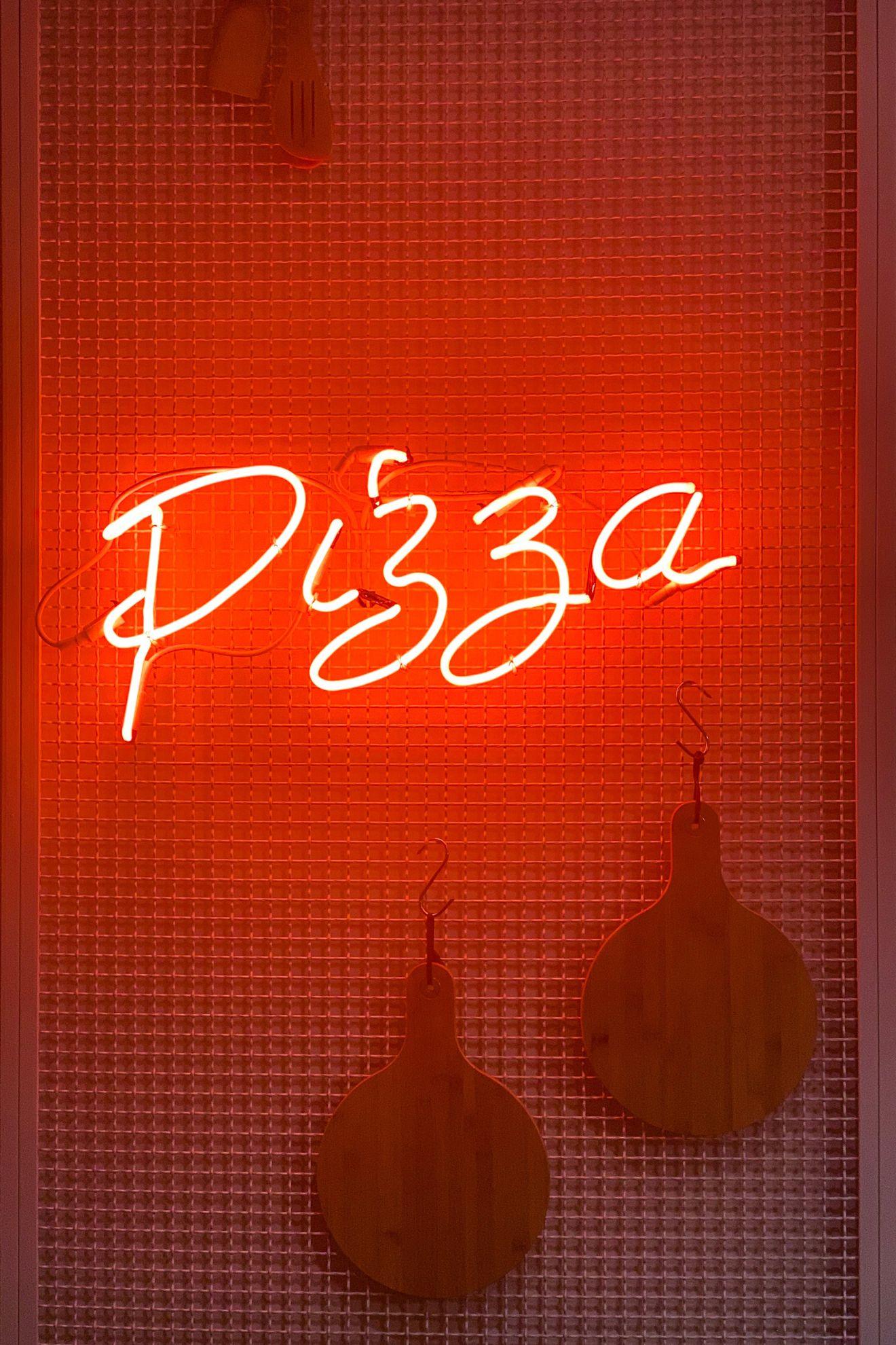 Un néon lumineux qui représente le mot "pizza" et des planches en bois.