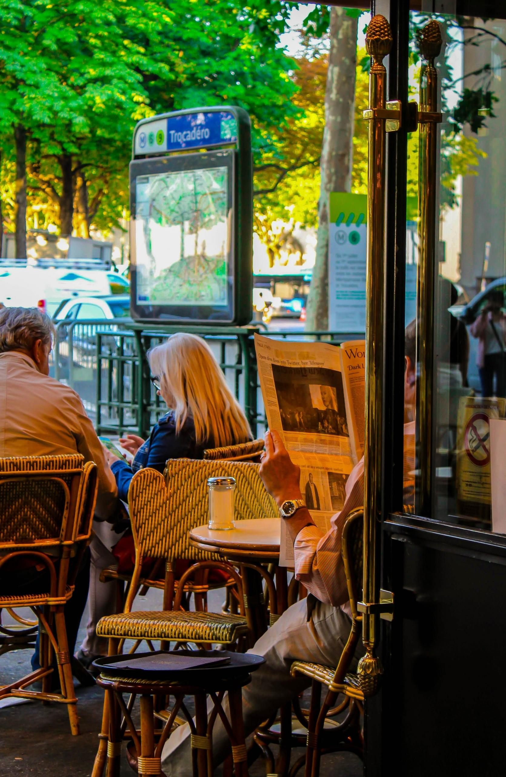 Un homme lit son journal en terrasse à Paris.