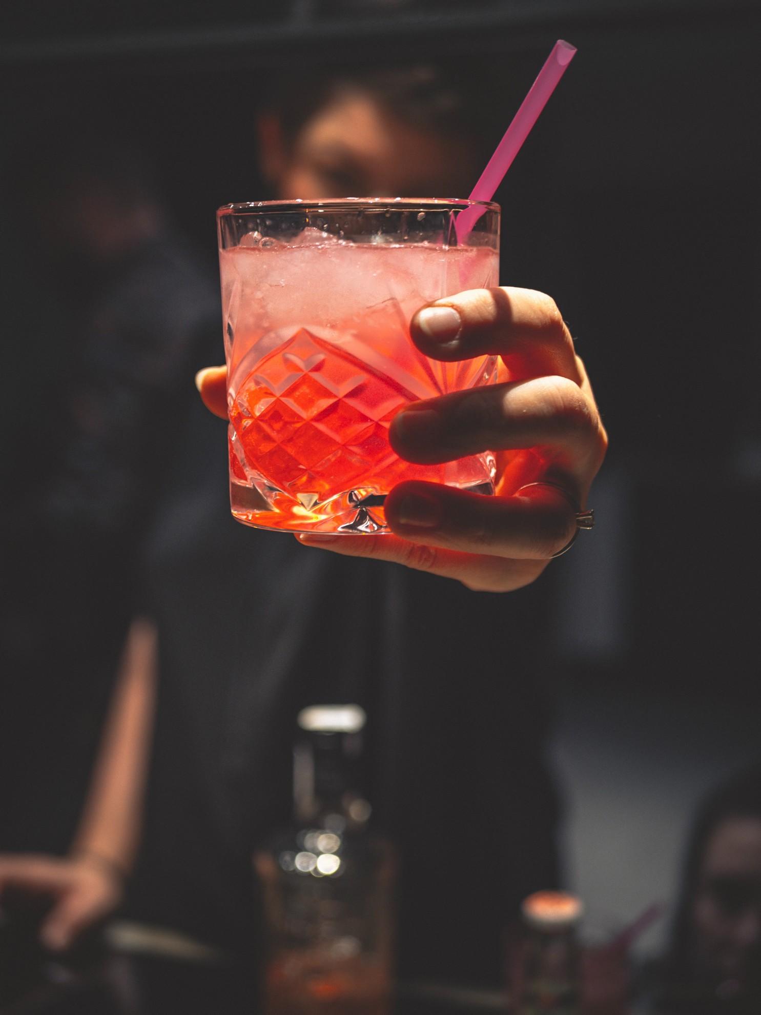 Un barman qui tend un cocktail rouge à un client.
