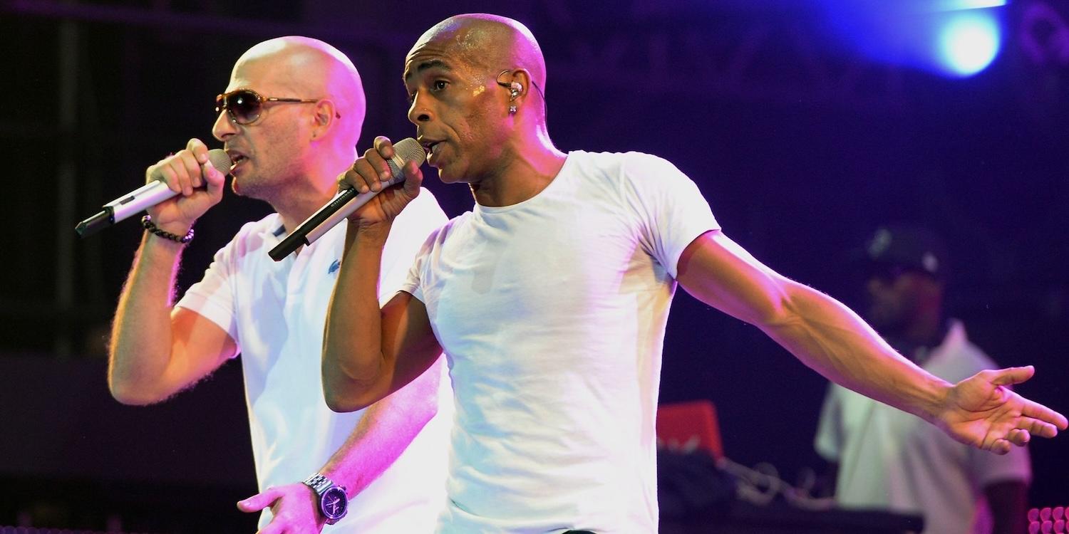 2 membres du groupe IAM en train de chanter sur scène avec un micro à la main.