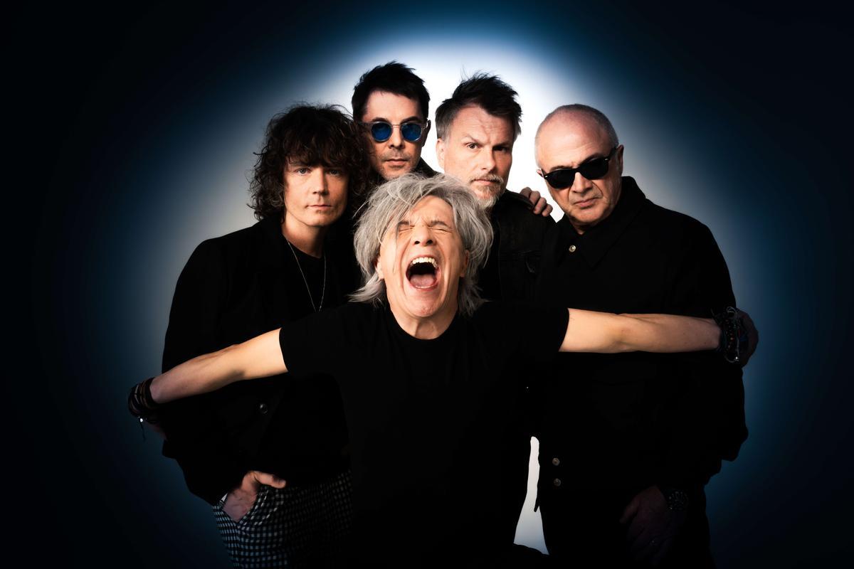 Le groupe Indochine debout dans un halo de lumière sur fond noir.