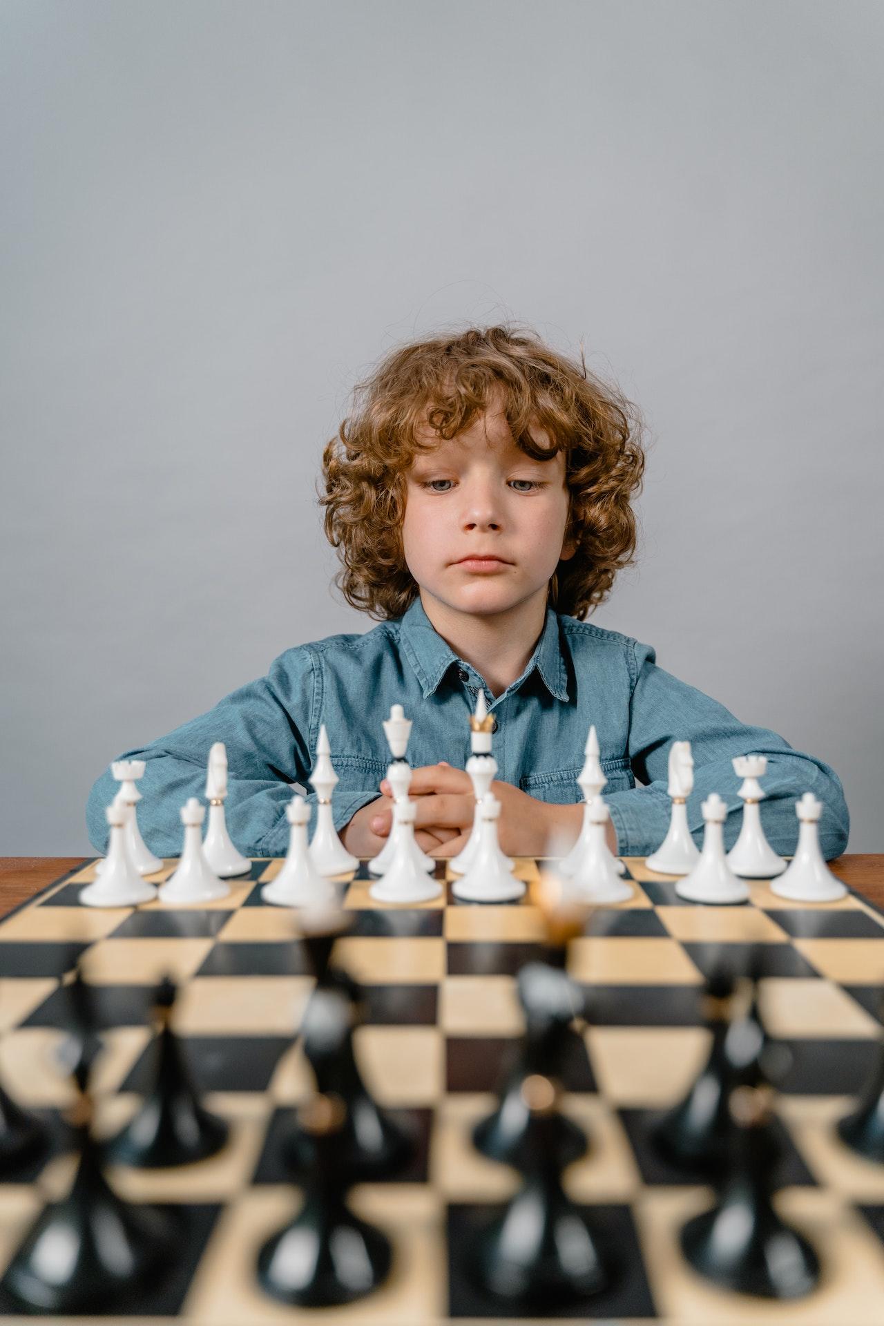 Un enfant aux cheveux blonds joue aux échecs.