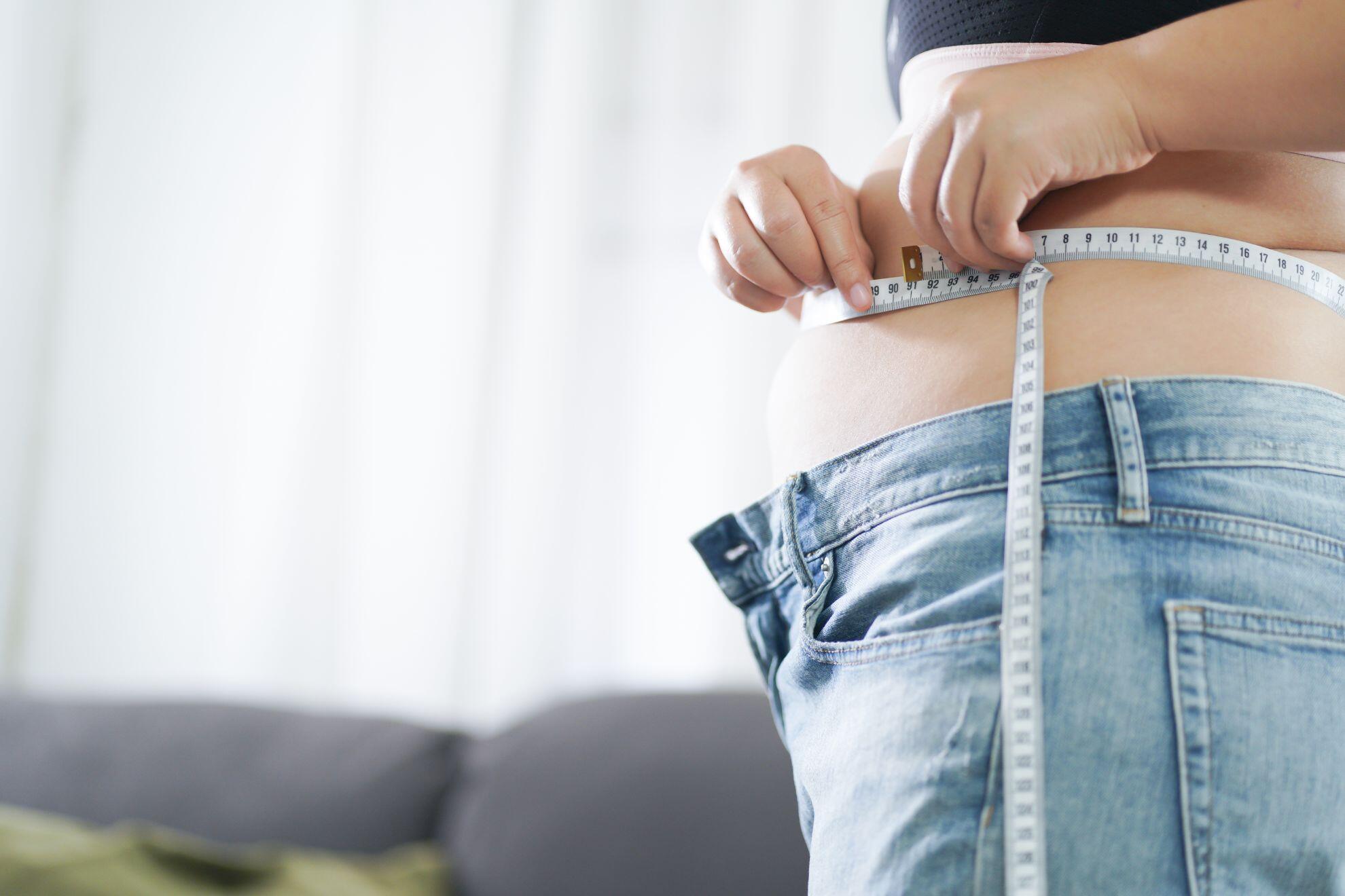 Une personne en train de mesurer son tour de taille avec un mètre ruban.