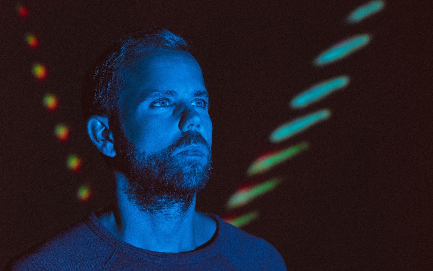 Le visage d'Anthony Gonzalez est éclairé par une lumière bleue sur un fond noir.