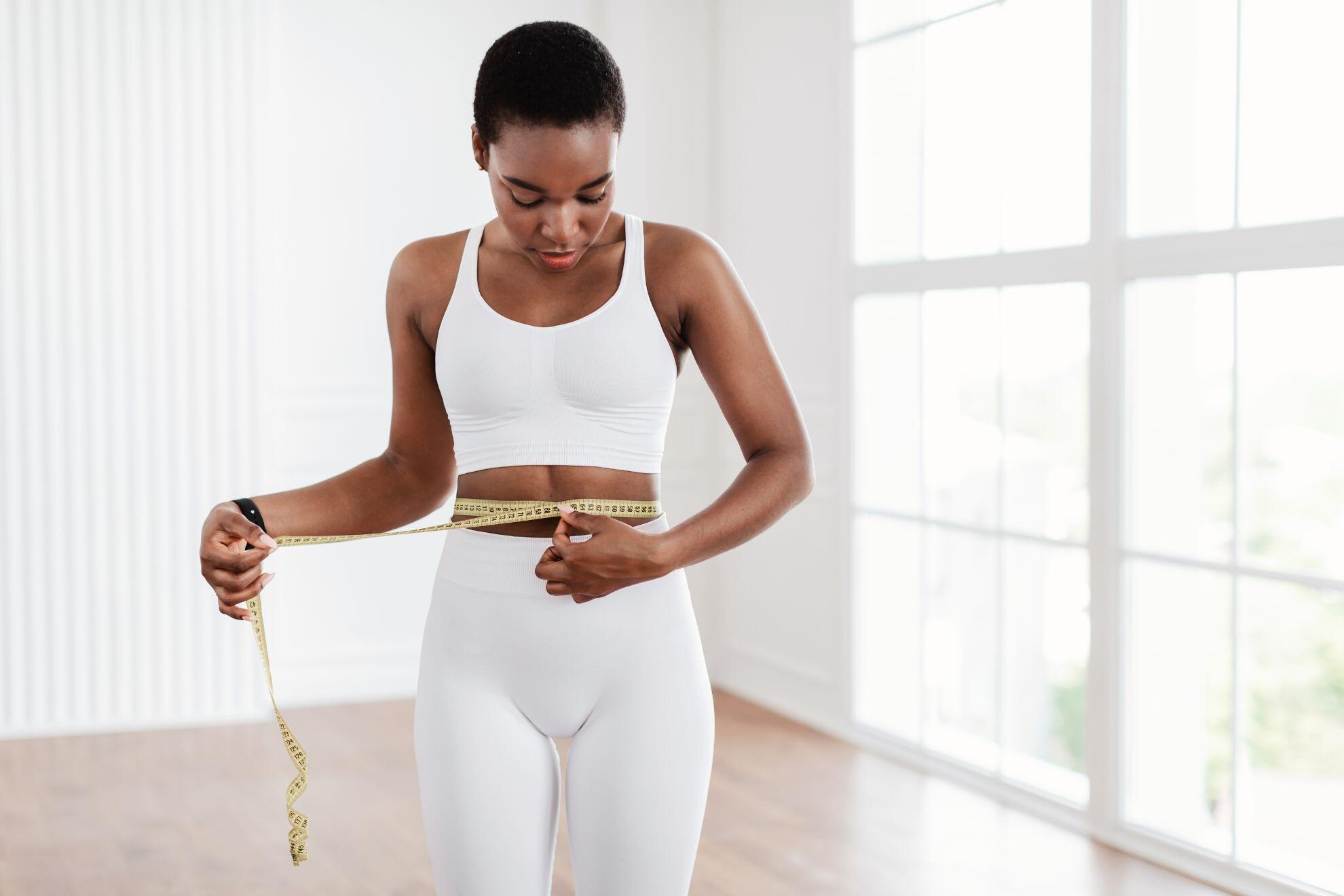Une femme en train de mesurer son tour de taille.