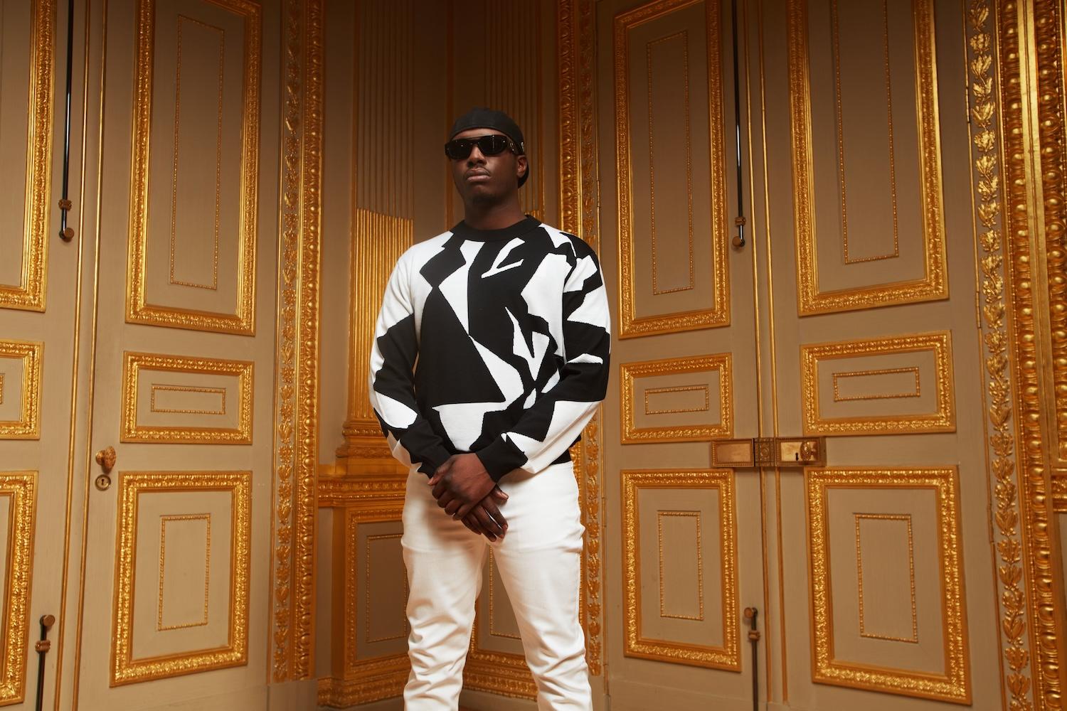 Le rappeur Werenoi est debout dans une pièce au décor ancien.