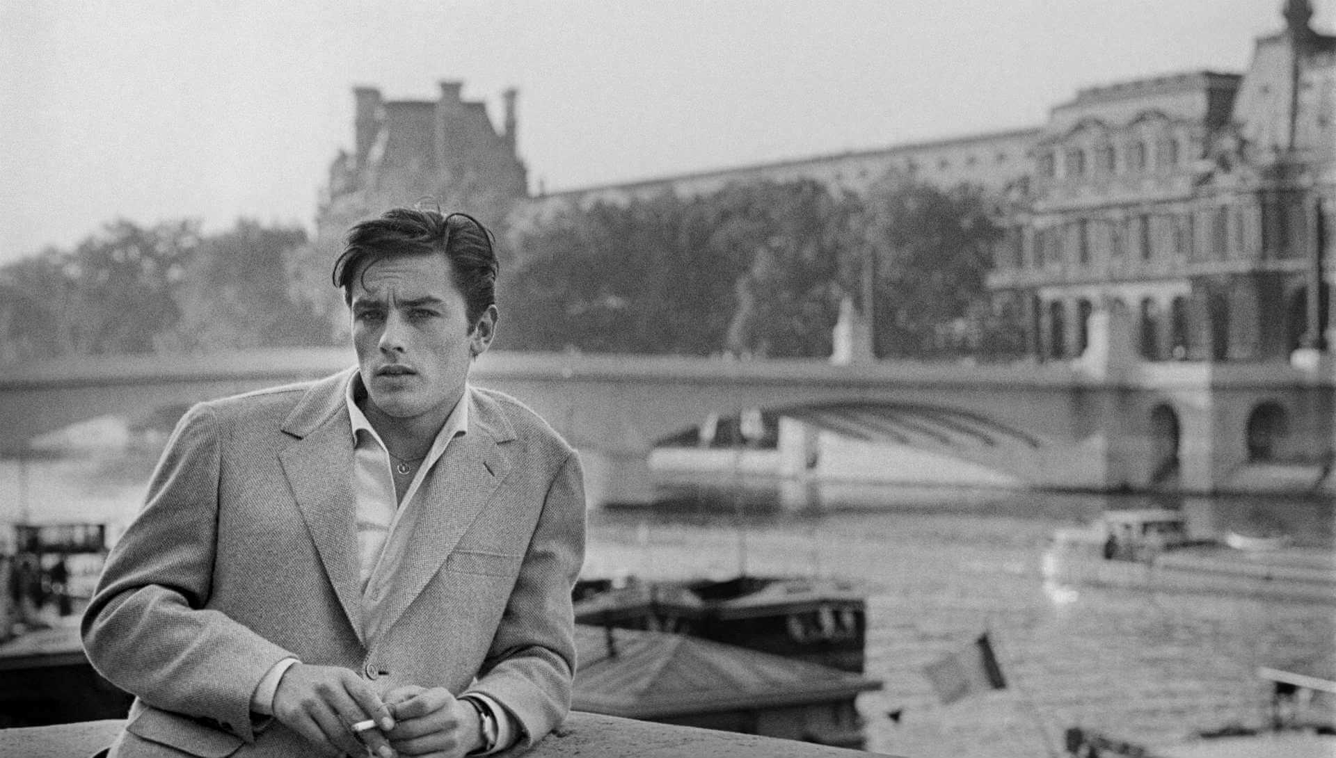 Une photo d'Alaine Delon en noir et blanc sur un pont de Paris.