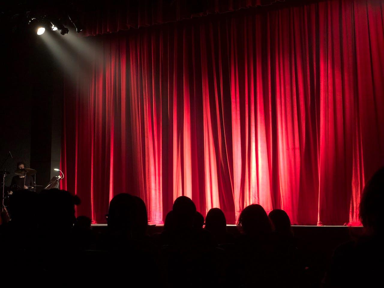Salle de théâtre avec rideaux rouges fermés.