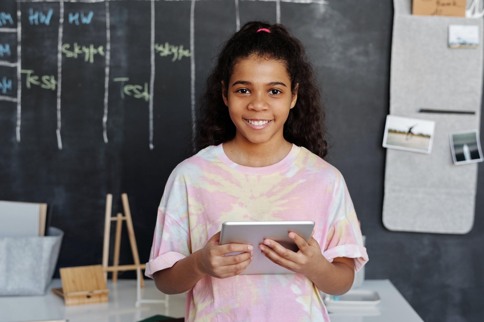 Une jeune fille avec une tablette dans les mains dans une salle de classe.