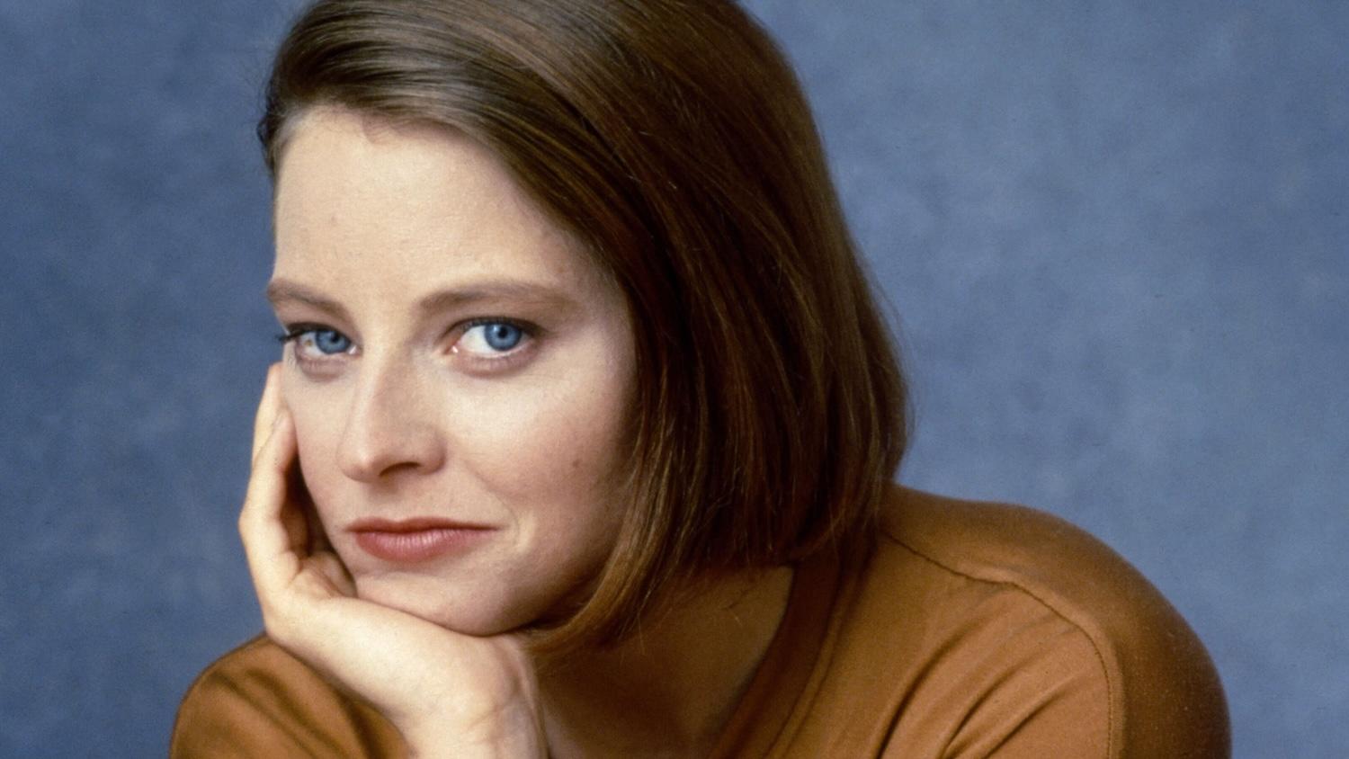 Jodie Foster de face avec la main sous son menton.