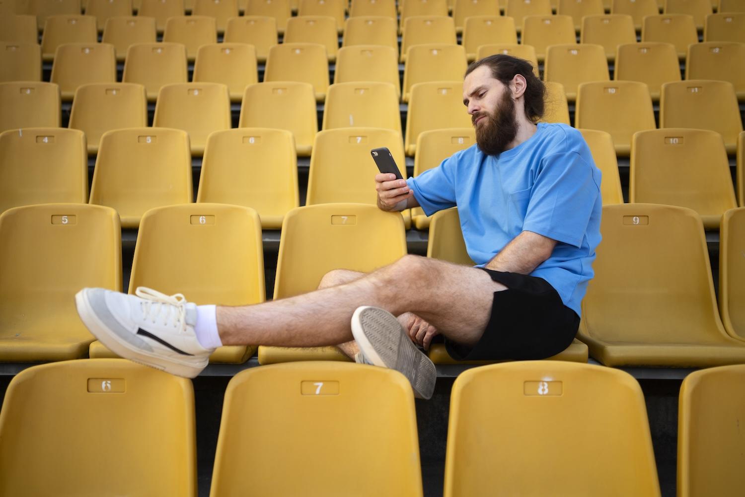 Un monsieur est assis dans la tribune et regarde son téléphone.