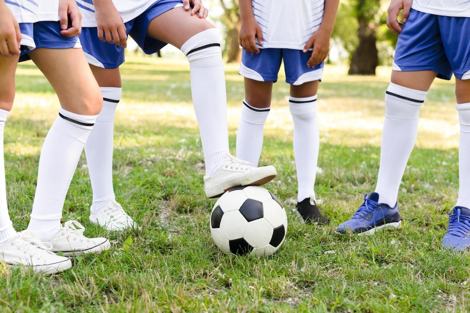 Des enfants en tenue de foot sont regroupés autour d'un ballon de foot.