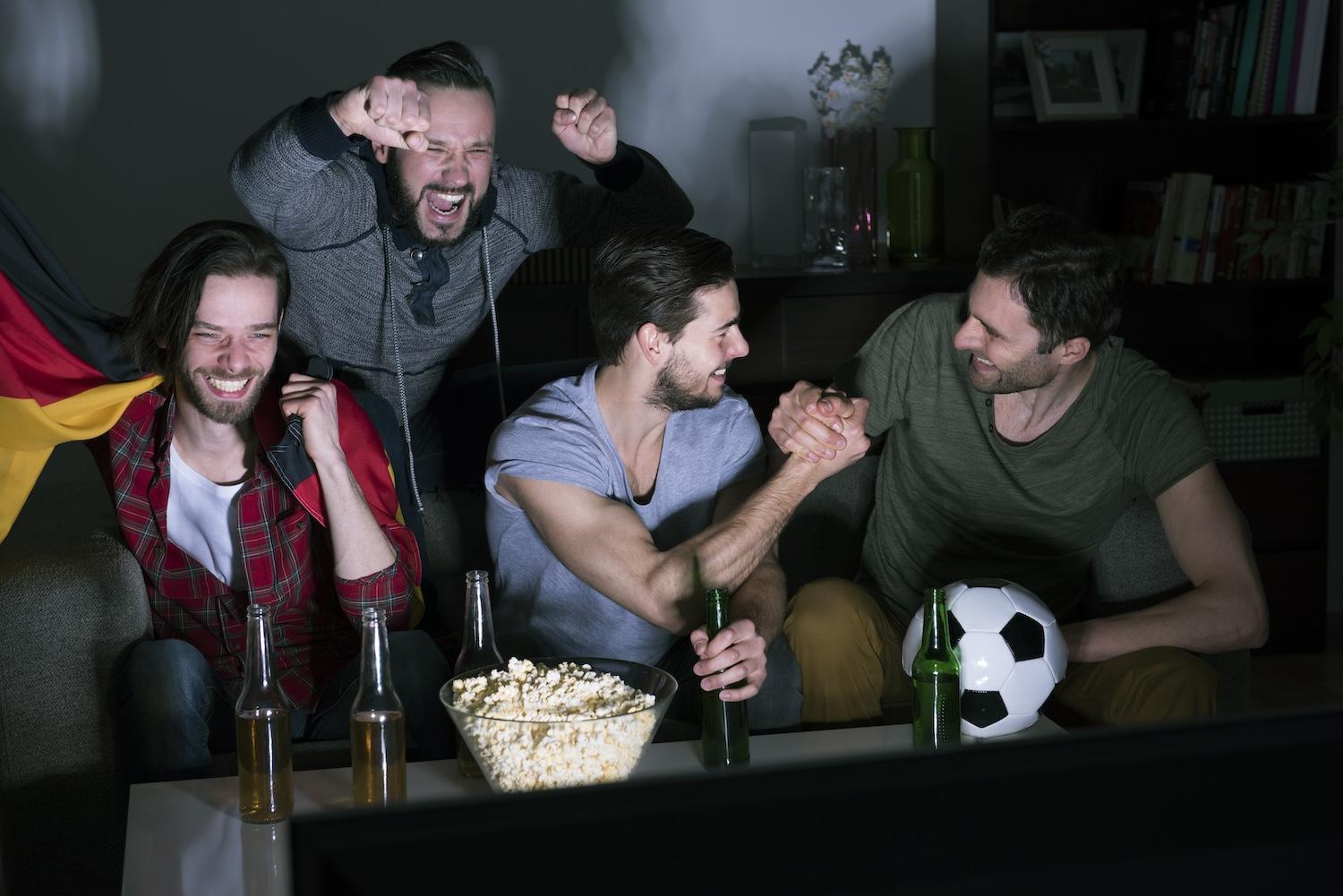 Plusieurs hommes sont sur un canapé et regardent un match de foot en buvant de la bière.
