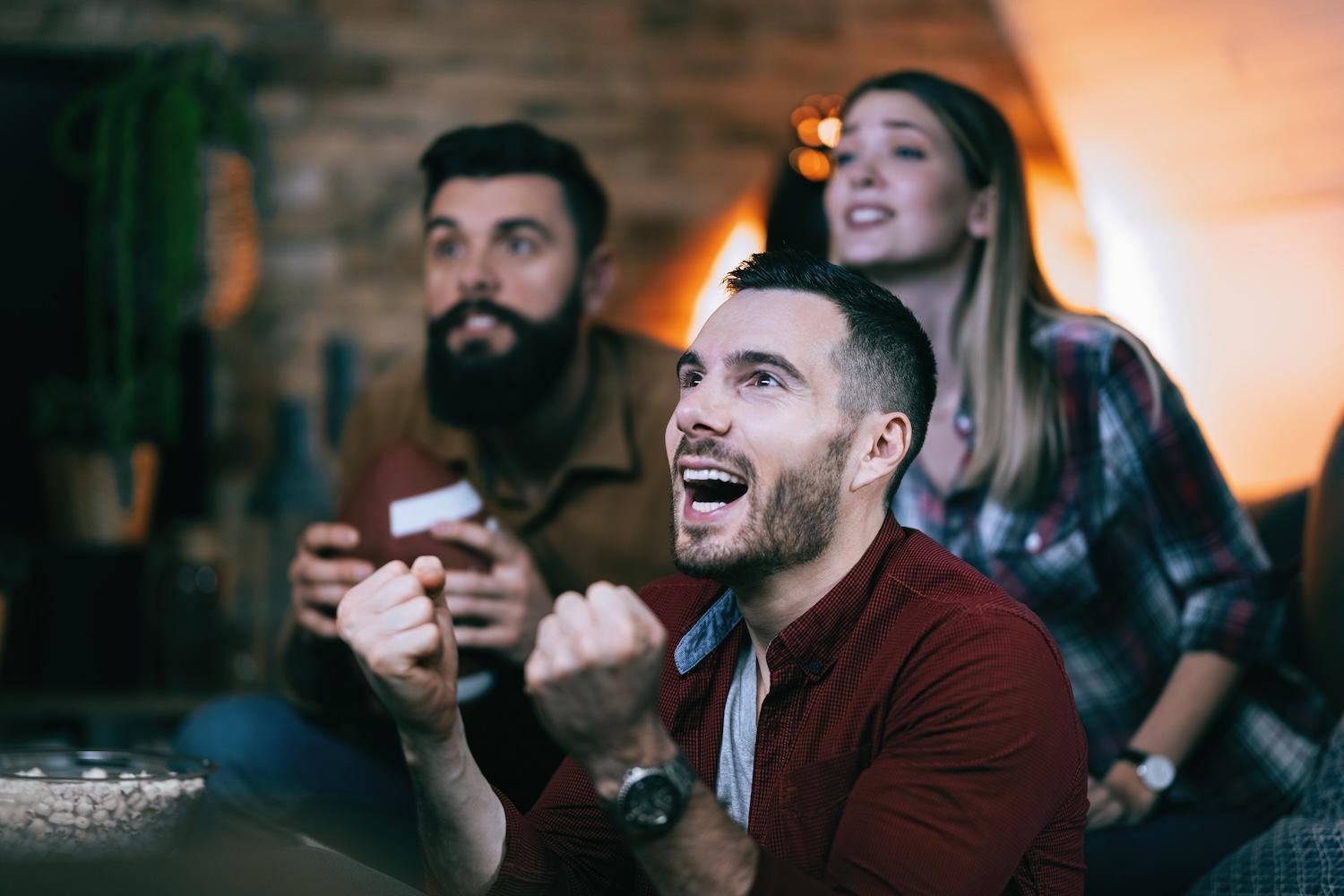 3 jeunes adultes sont en train de regarder un match à la télé.
