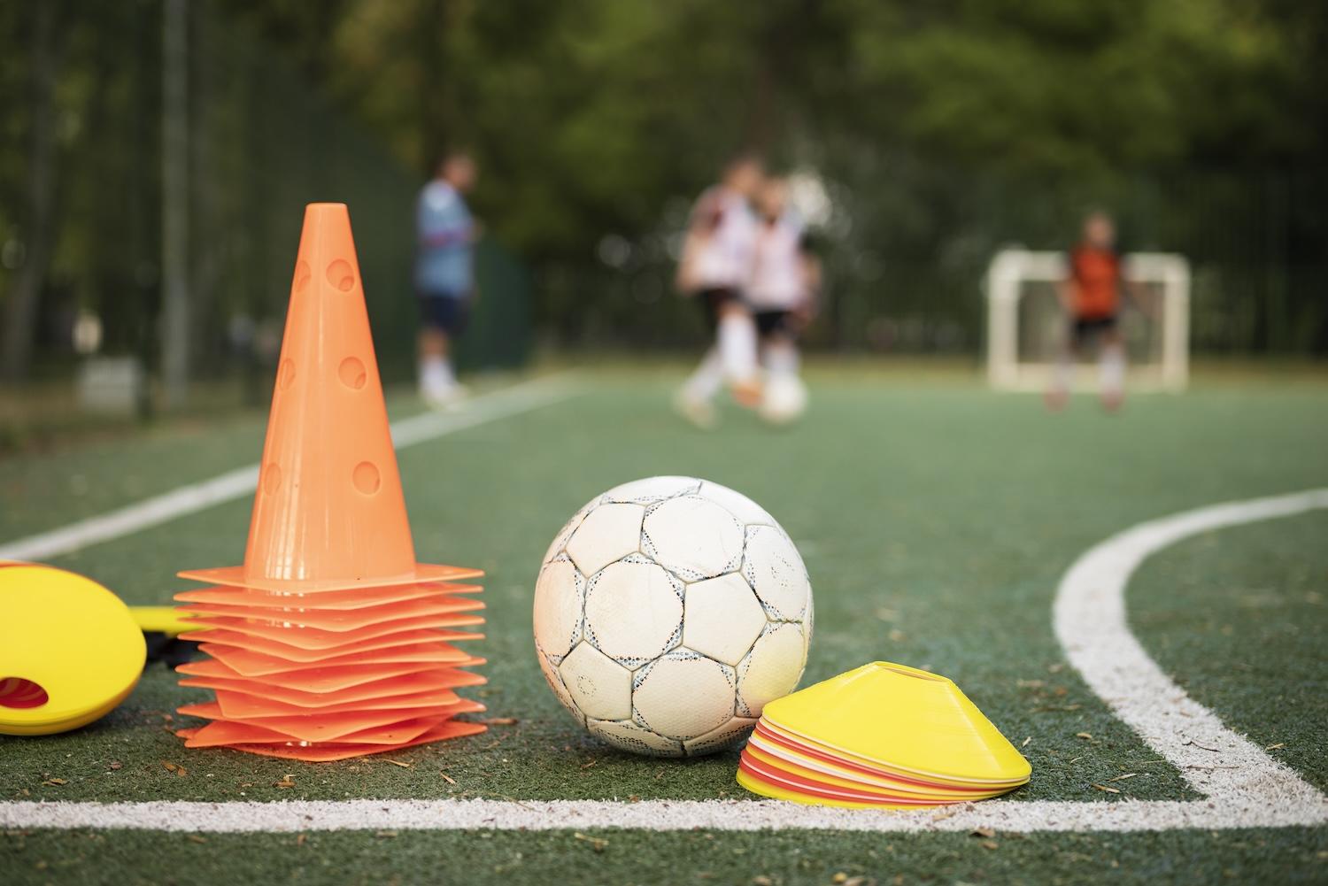 Entraîneur de foot qui enseigne à ses élèves avec des plots au premier plan.