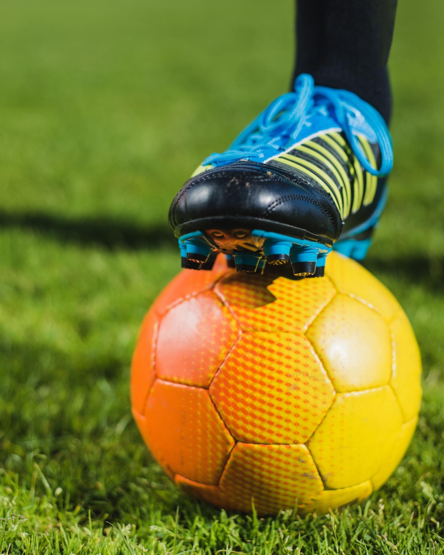 Un pied avec des crampons est posé sur le ballon de foot.