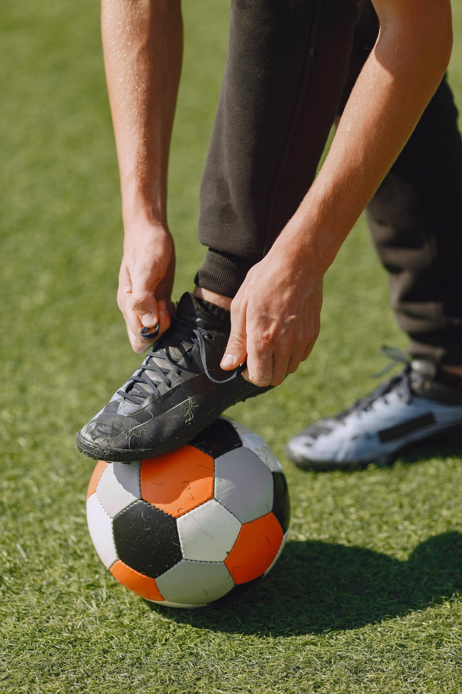 Joueur de foot qui lace sa chaussure de foot posée sur un ballon.