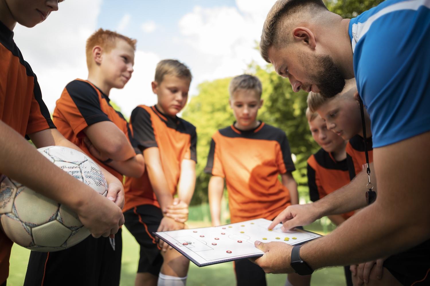 De jeunes joueurs sont regroupés autour d'un entraineur de foot.