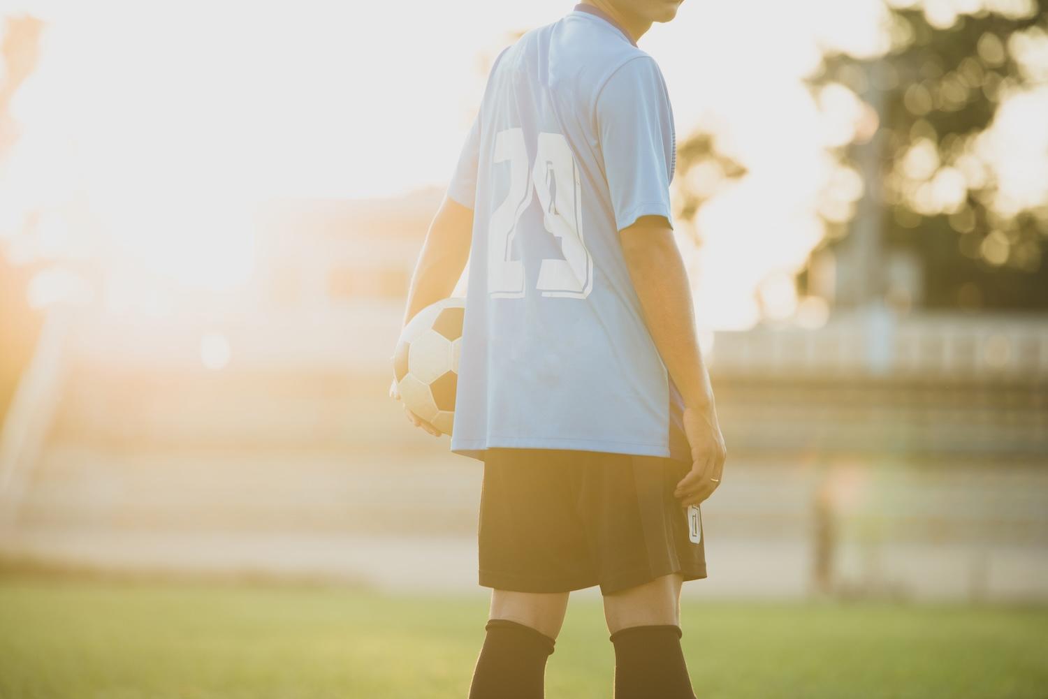 Joueur de foot au coucher du soleil avec un ballon à la main.