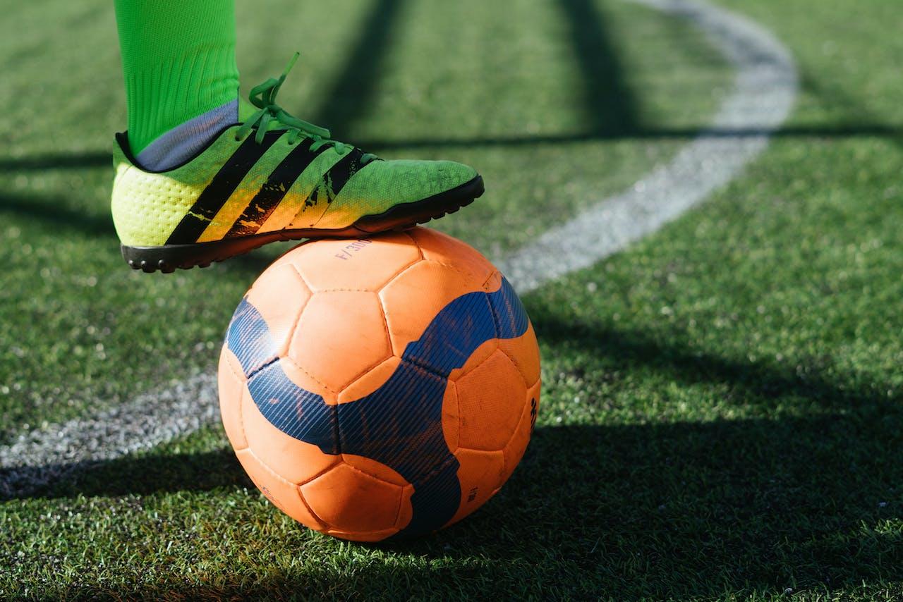 Pied posé sur un ballon de football orange et bleu. 