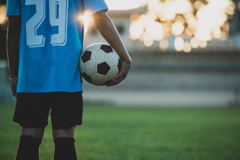 Une personne tient un ballon au bout de son bras le long de son corps sur un stade.
