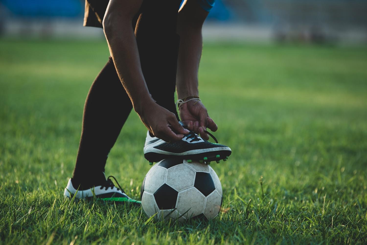 Un joueur refait ses lacets sur un ballon de foot.