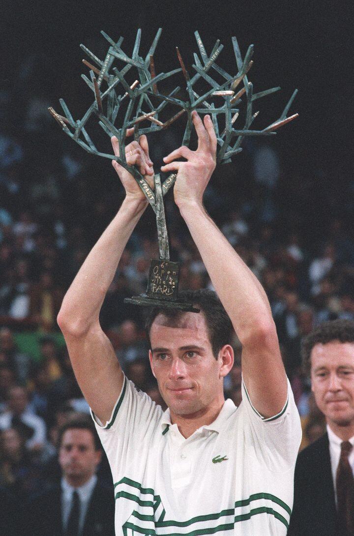 Photo de Guy Forget soulevant un trophée de tennis. 