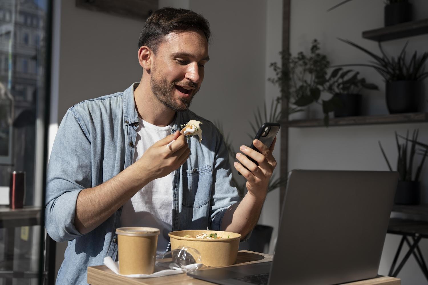 Un homme en train de manger et de regarder le foot en streaming sur son smartphone.