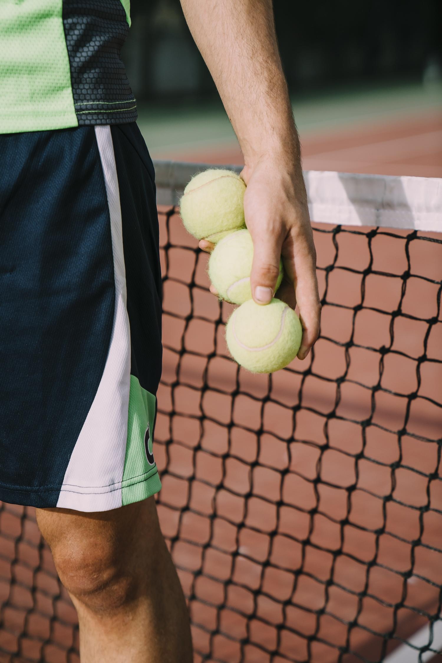 Un joueur de tennis tient 3 balles dans sa main devant le filet.