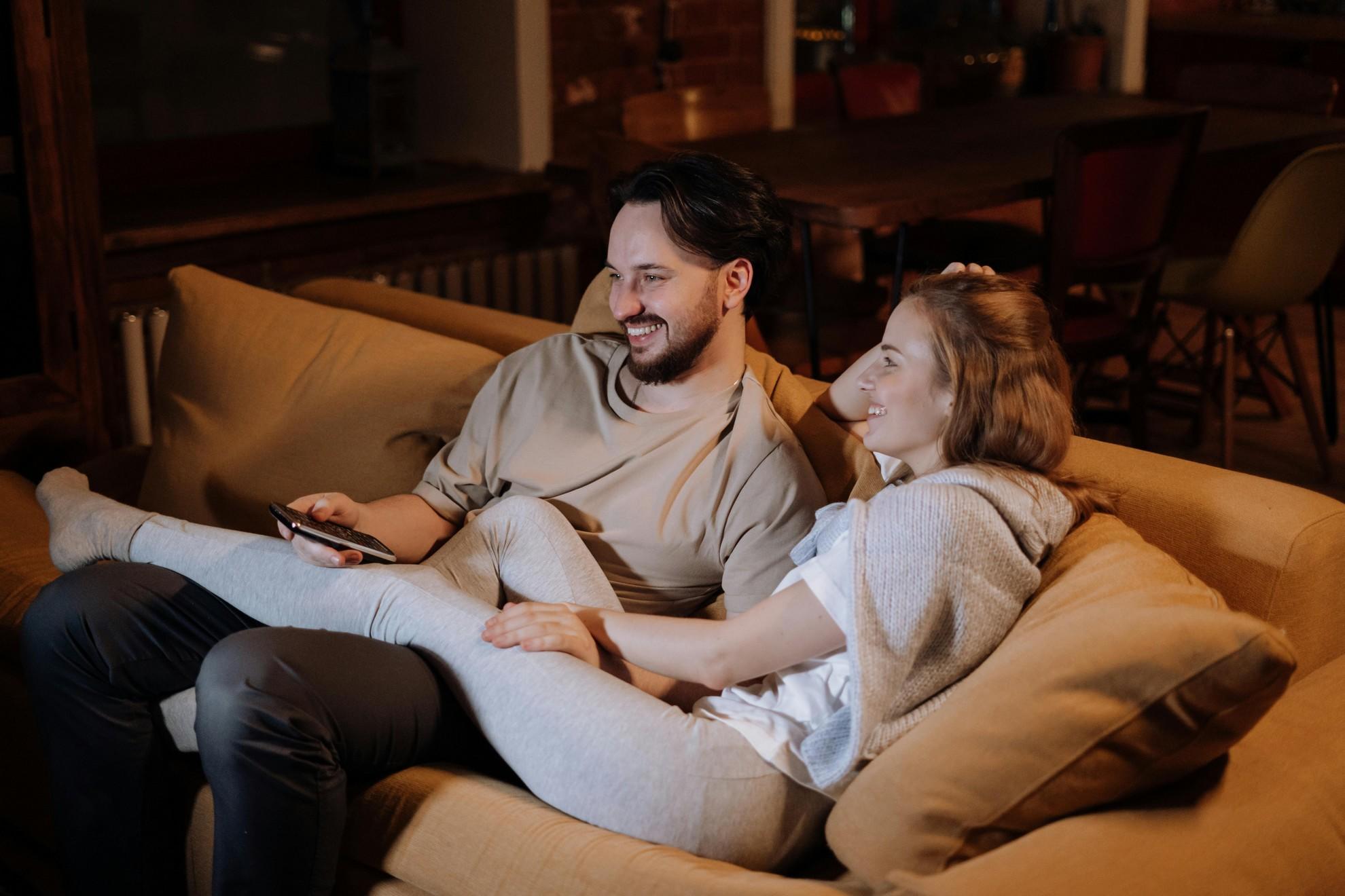 Un couple sur son canapé en train de regarder la télévision.