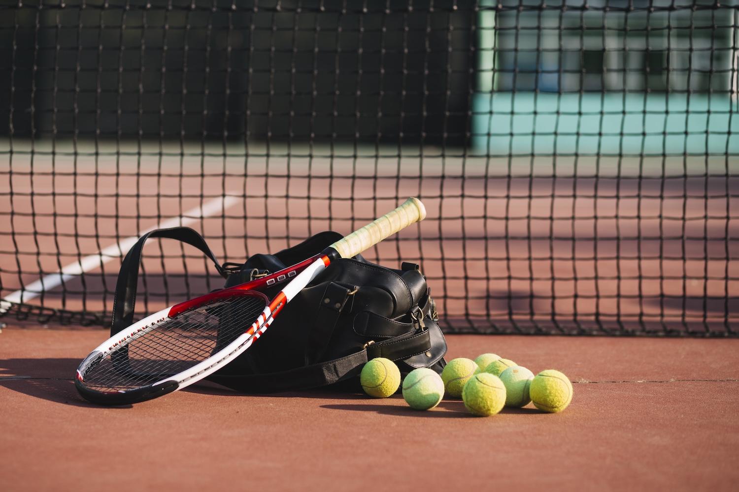 Un sac de tennis est posé sur un court avec une raquette dessus et des balles à côté.