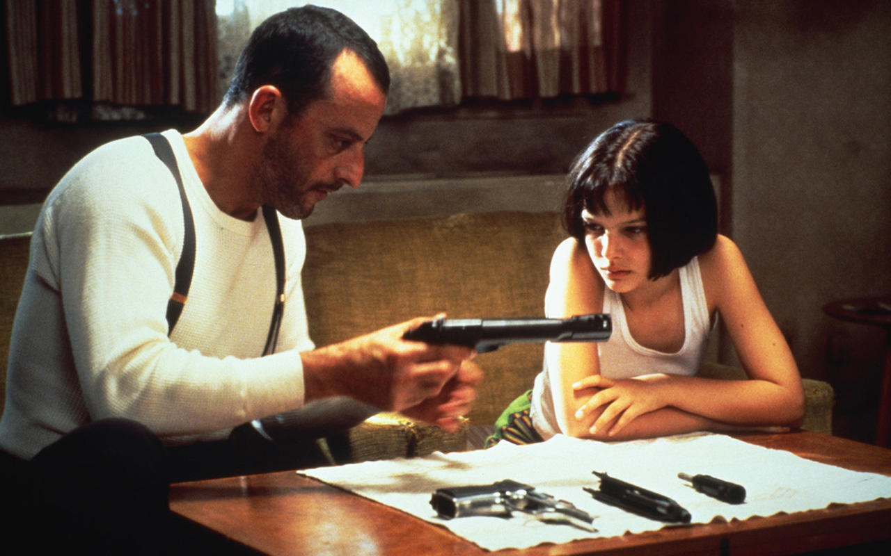 Un homme tient une arme dans sa main et une jeune fille le regarde manier l'arme.