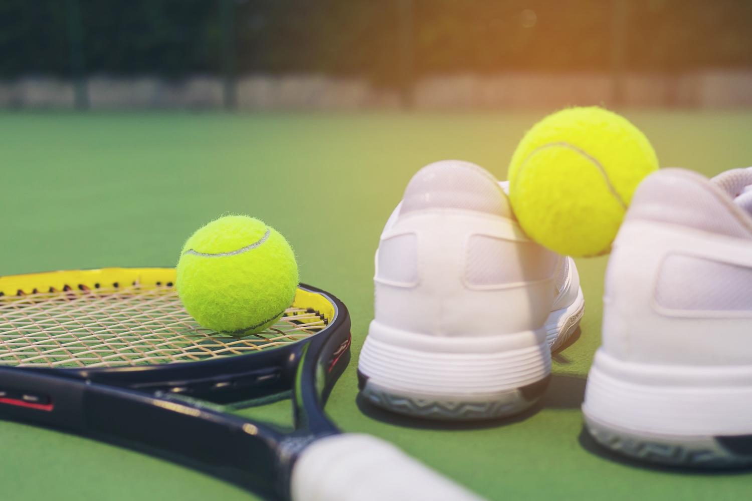Des chaussures de sport, une raquette et des balles sont posées sur un court.