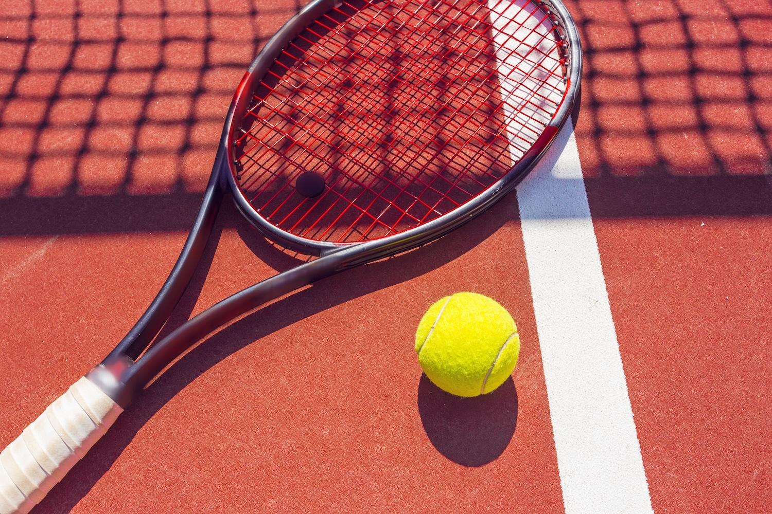 Une raquette de tennis est posée sur un court à côté d'une balle.