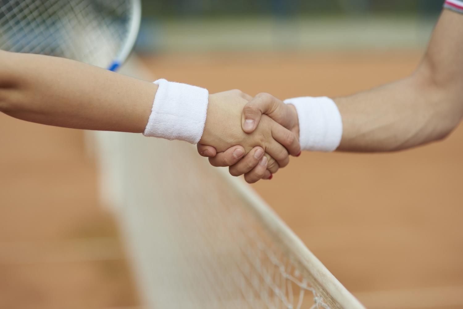 Deux joueurs de tennis se servent la main au-dessus du filet.