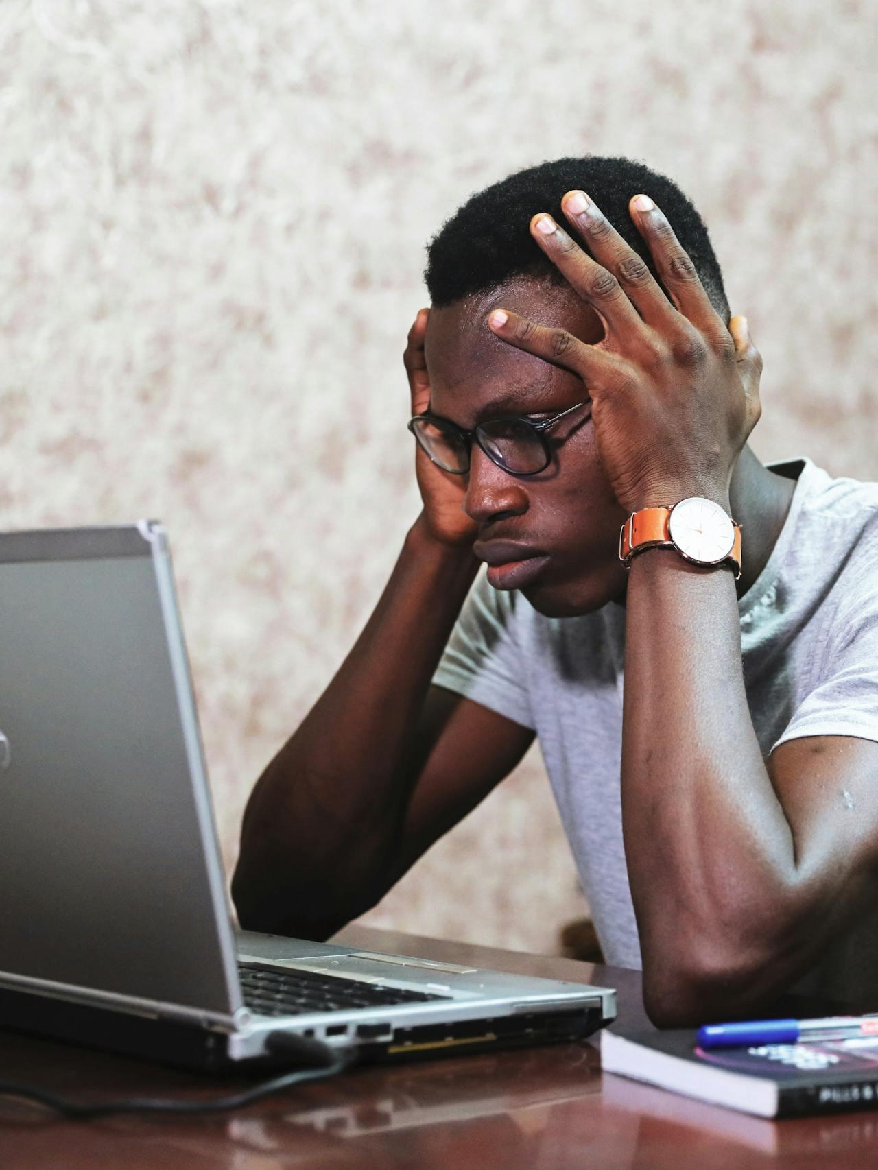 Photo d'un jeune homme noir assis devant son ordinateur la tête entre les mains, visiblement désespéré de ne pas comprendre Excel !