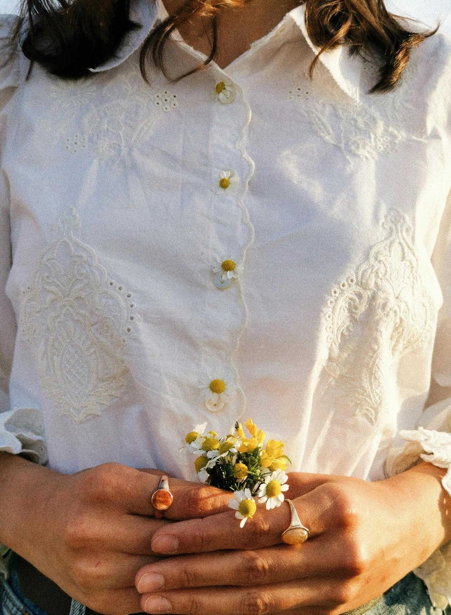 Une femme avec un chemisier blanc brodé et des marguerites.