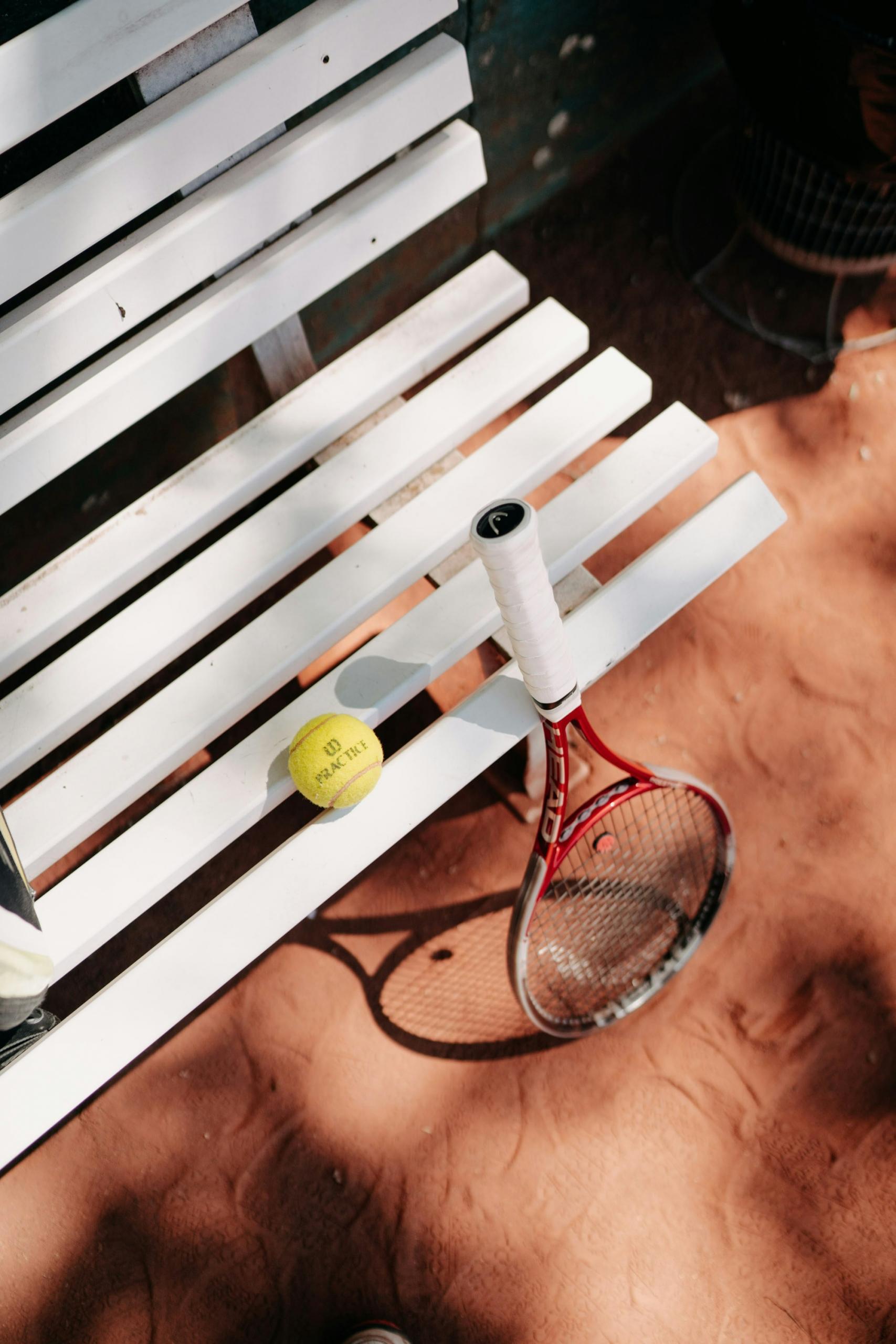 Une raquette et une balle de tennis posées sur un banc.