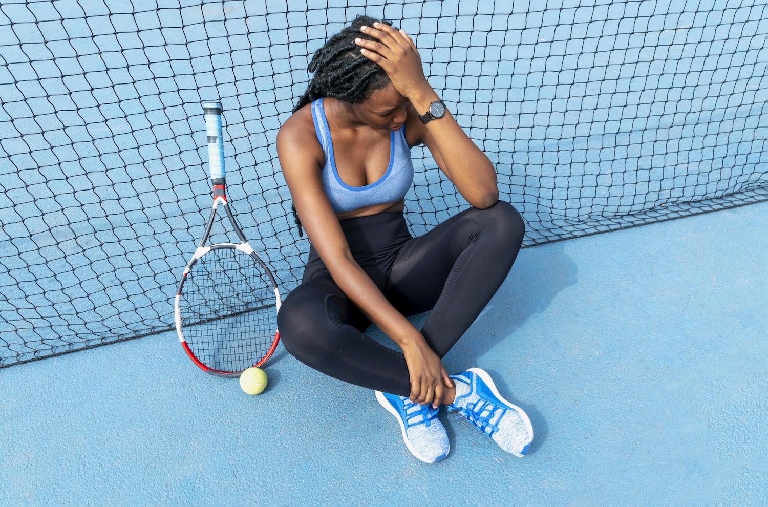 Une jeune joueuse de tennis est assise le long du filet avec sa raquette posée à côté.