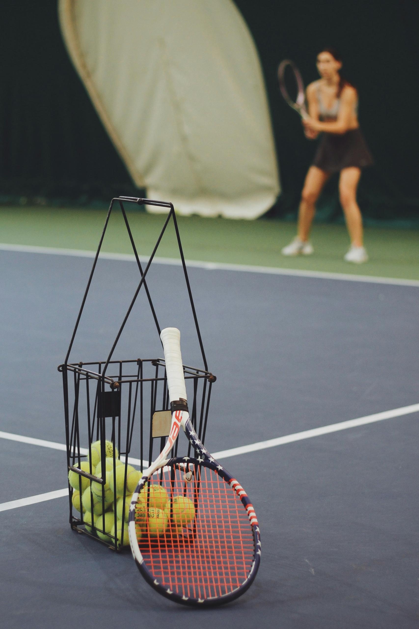 Une raquette de tennis posée contre un panier de balles.