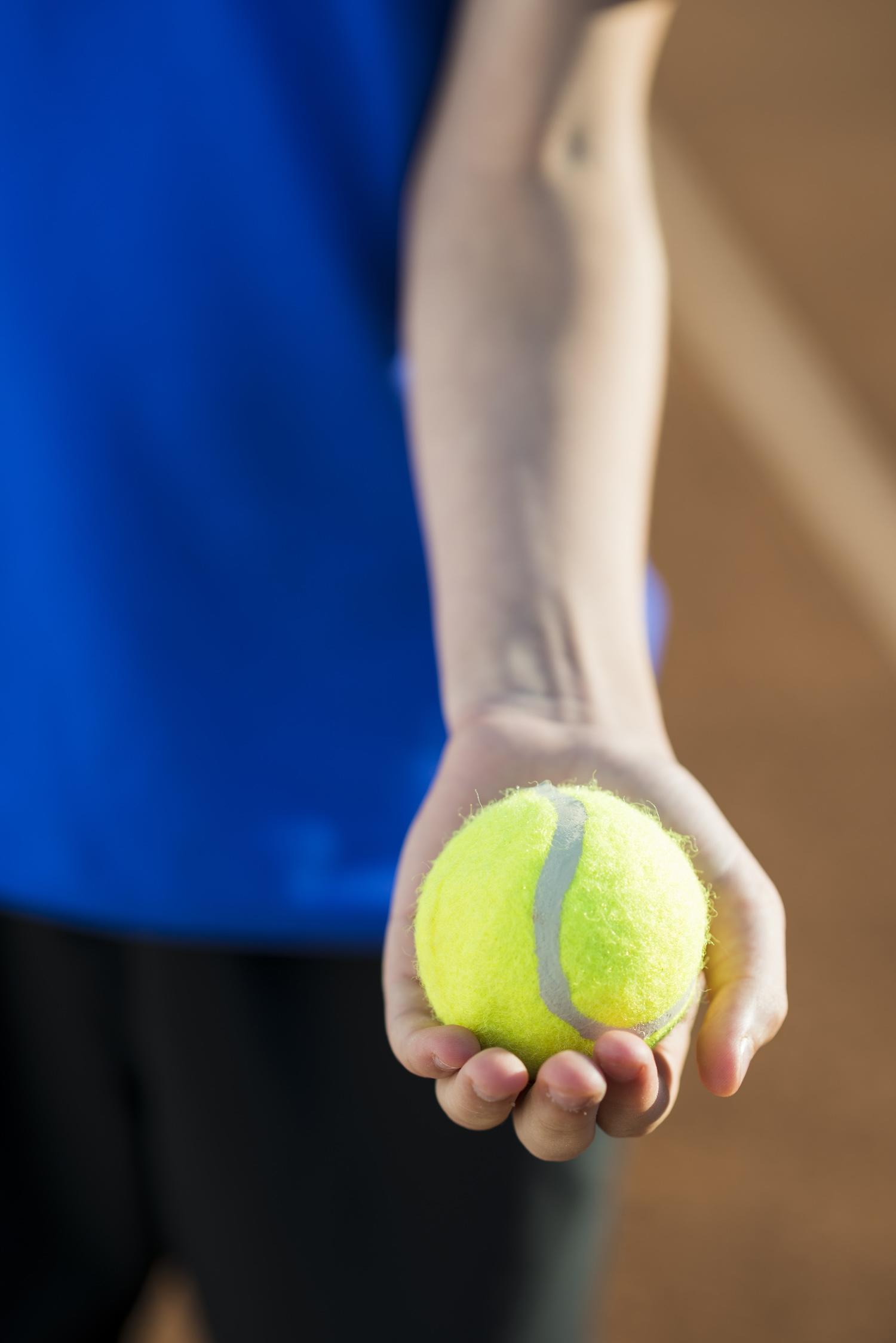 Un joueur tient une balle de tennis dans sa main.