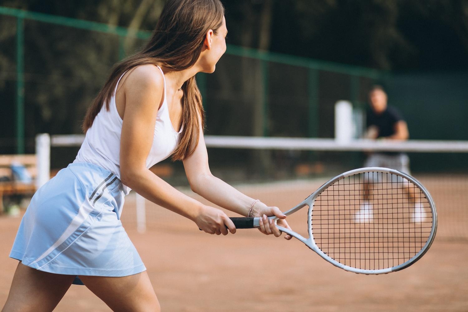 Une jeune femme tient une raquette de tennis et joue sur un court.