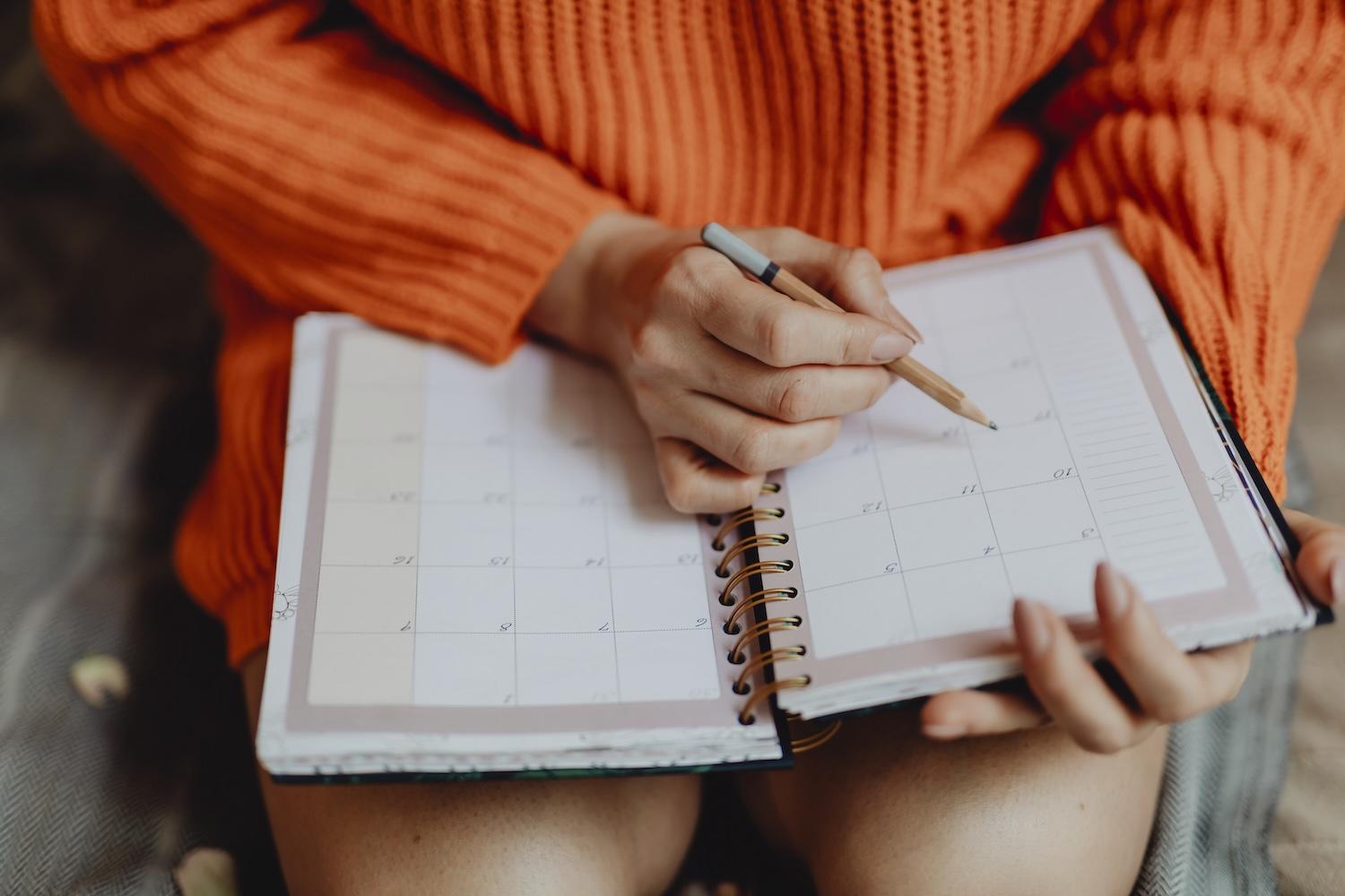 Une femme écrit dans son agenda ouvert sur ses genoux.