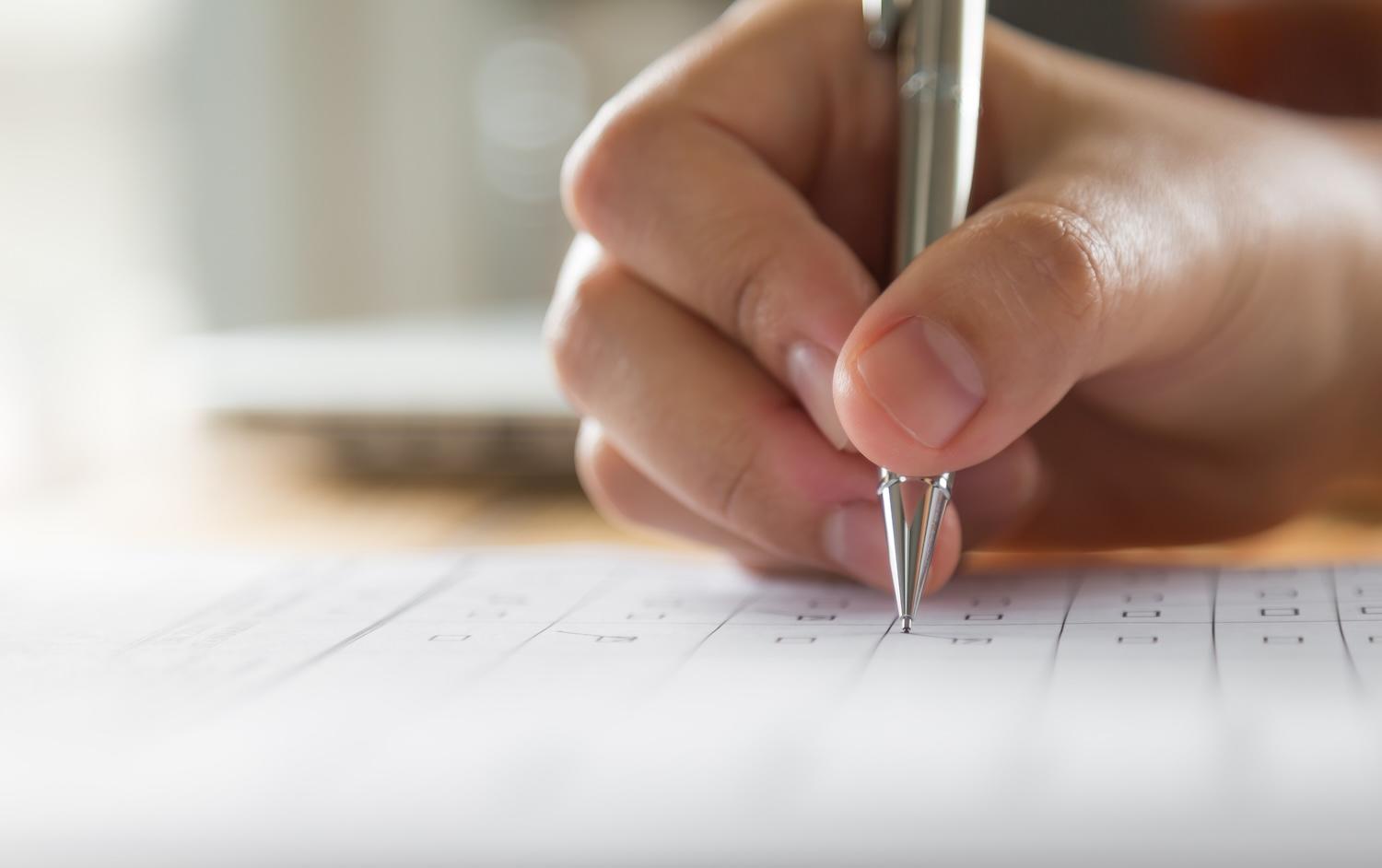 Une main est en train de remplir un questionnaire.