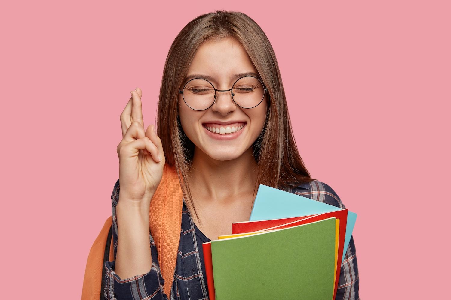 Une jeune femme tient des livres dans la main et croise les doigts.