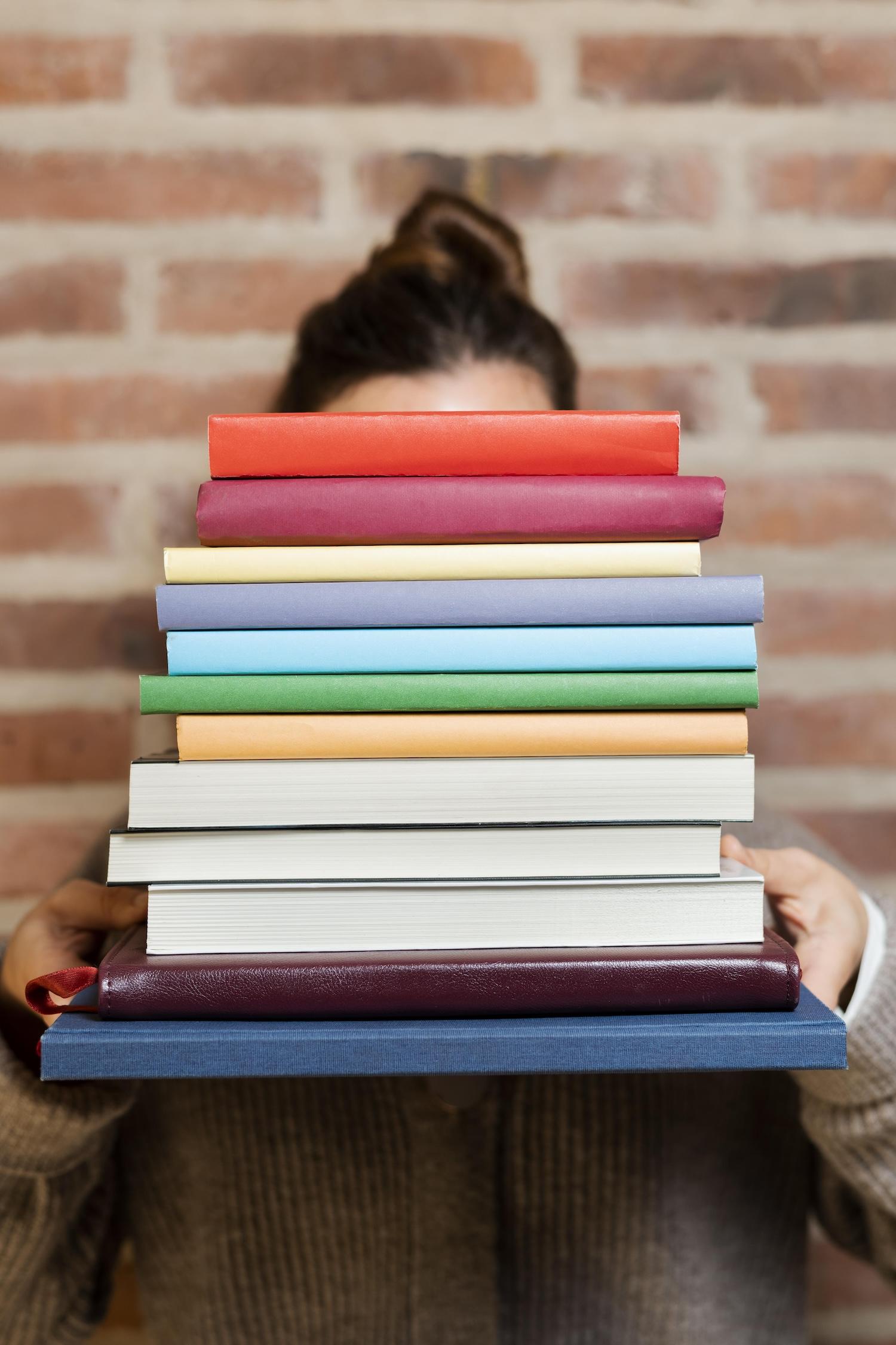 Une jeune femme tient une pile de livres devant elle.