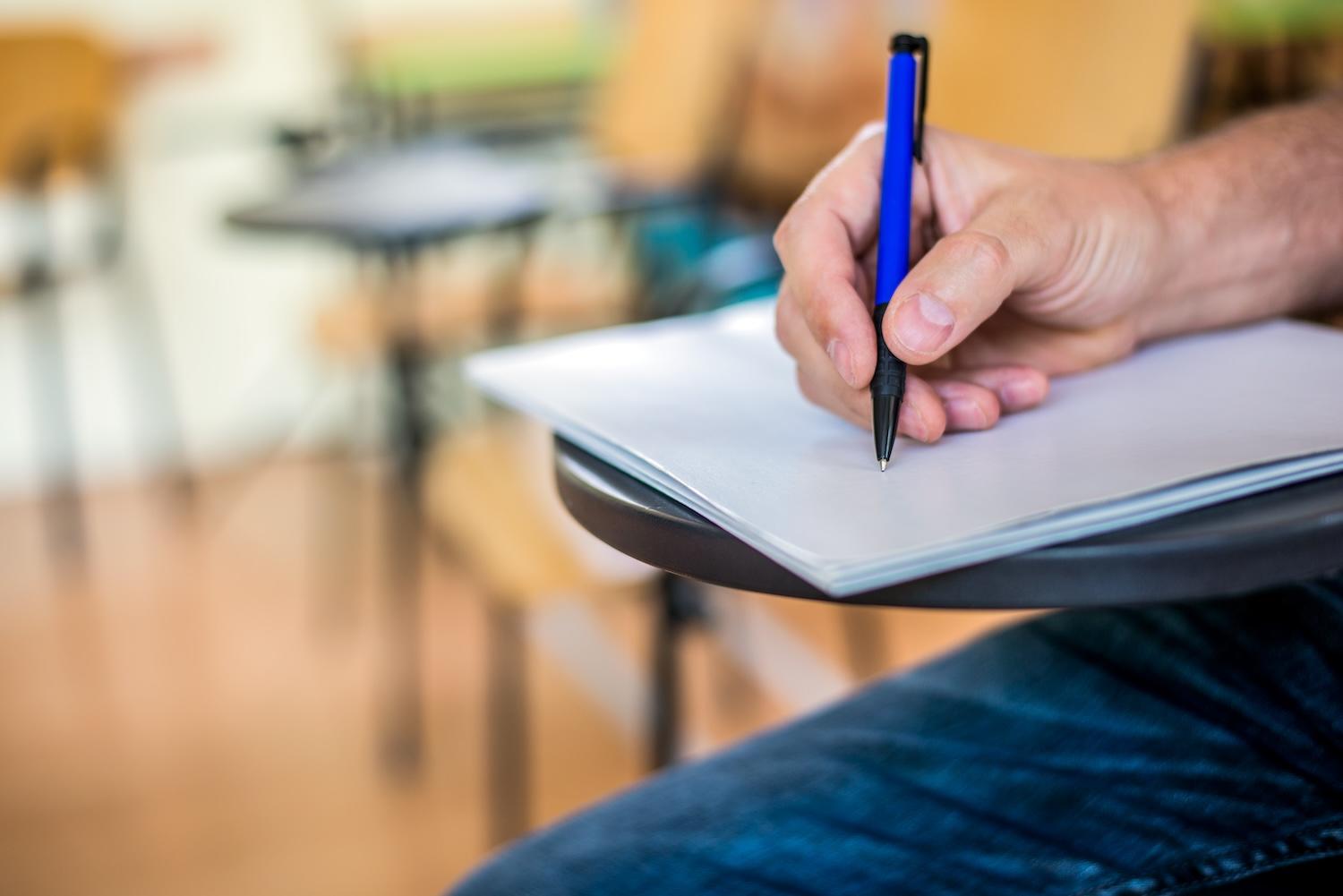Un homme écrit sur une feuille pendant un examen.