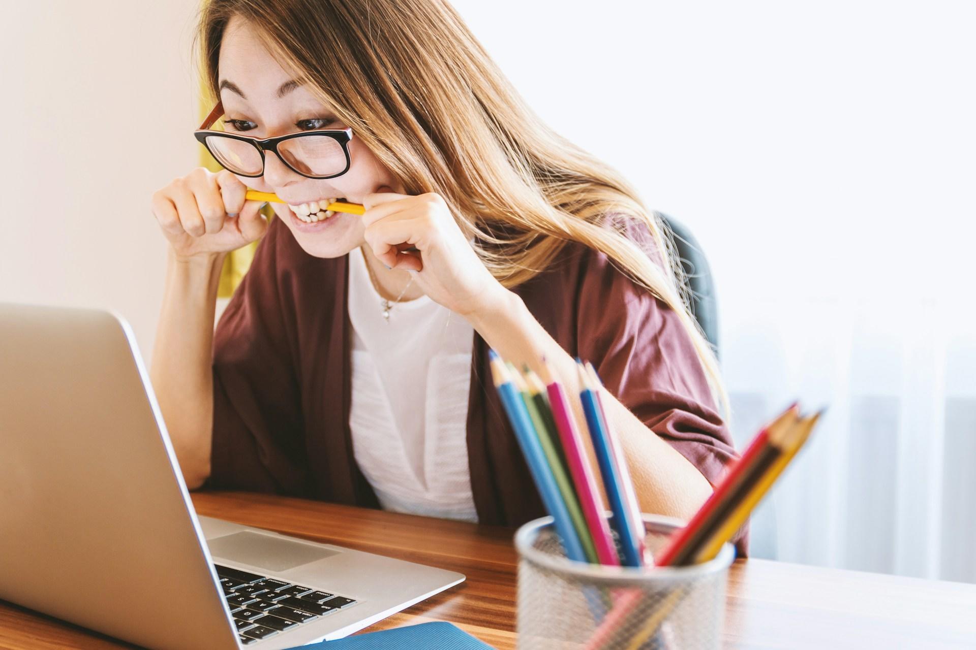 jeune femme en train de ronger un crayon devant son ordinateur