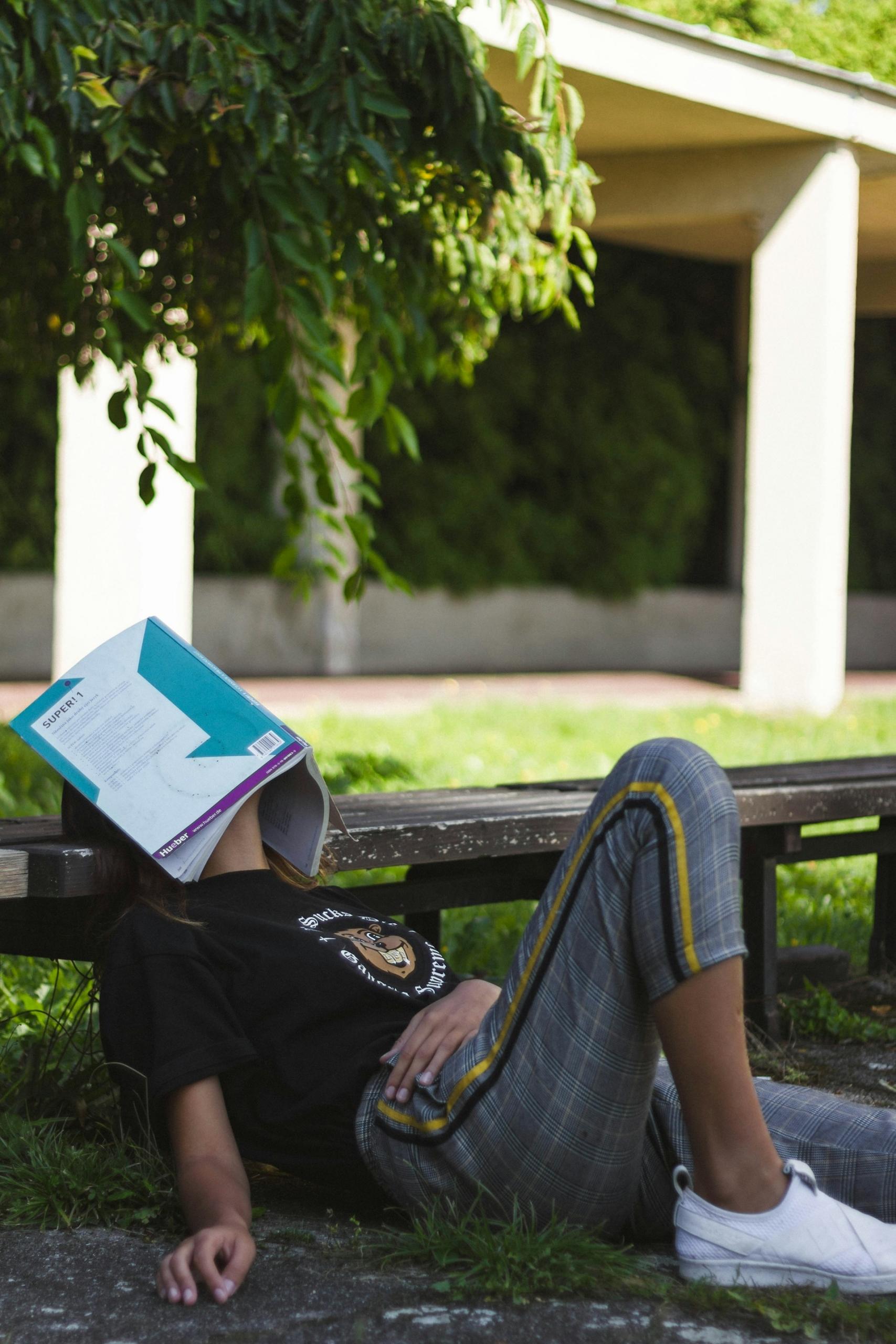 étudiant en train de réviser dans un parc avec un livre sur la tête 